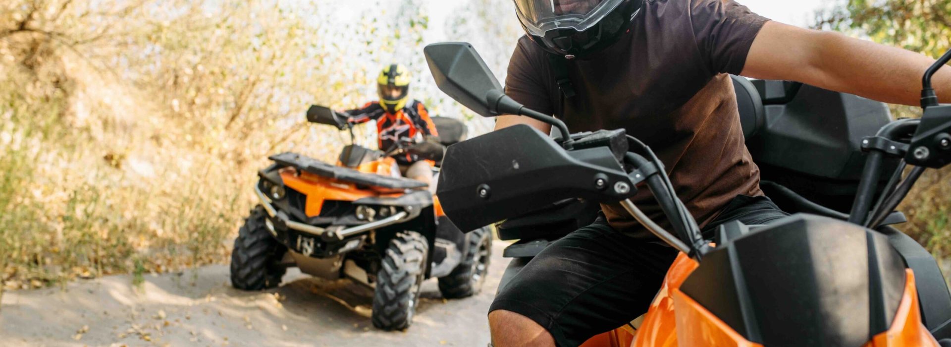 Two quad bike riders in helmets travels in forest, front view. Riding on atv, extreme sport and travelling, quadbike adventure