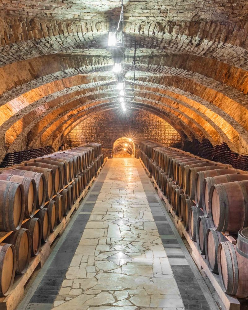 Old wooden barrels with wine in the ancient medieval stone cellars. Aged wine in barrels in underground cellar