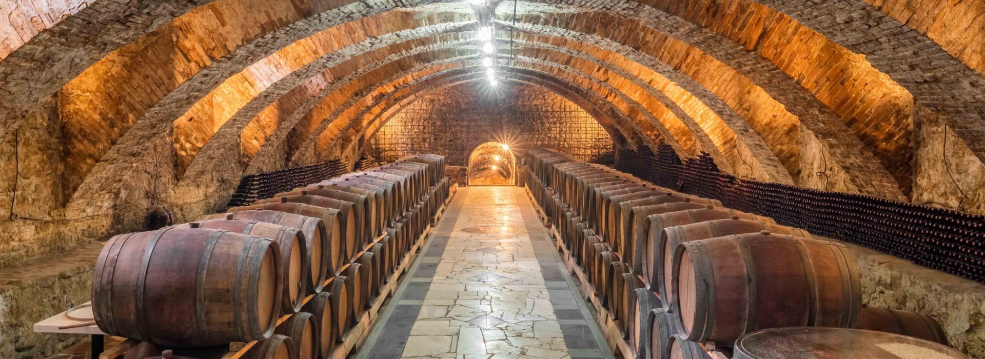 Old wooden barrels with wine in the ancient medieval stone cellars. Aged wine in barrels in underground cellar
