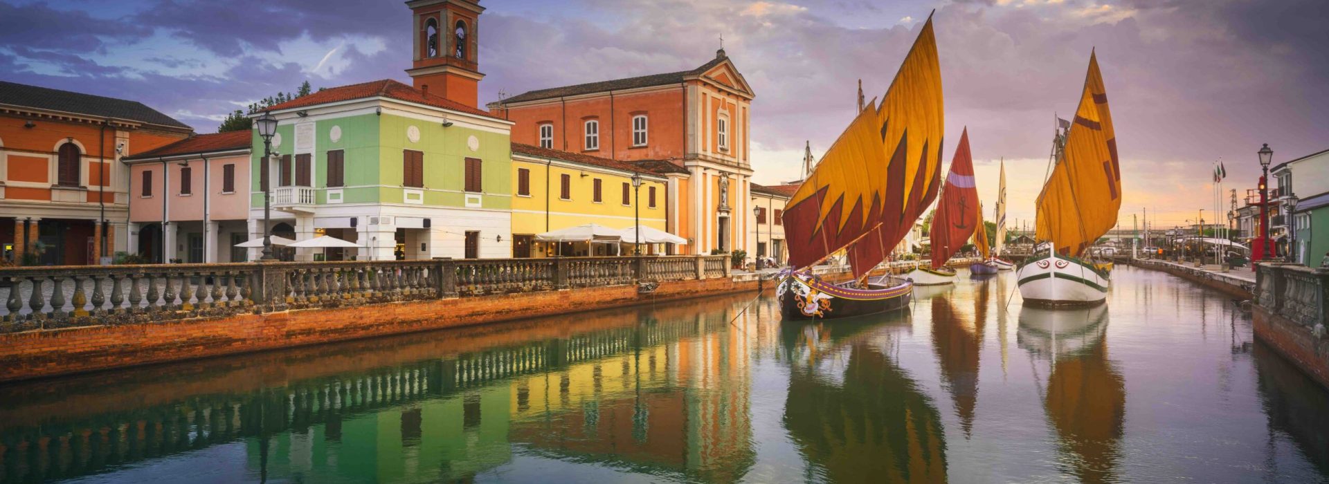 Cesenatico canal, historic wooden sailboats and church at sunset. Emilia Romagna region, Forlì Cesena province, Italy