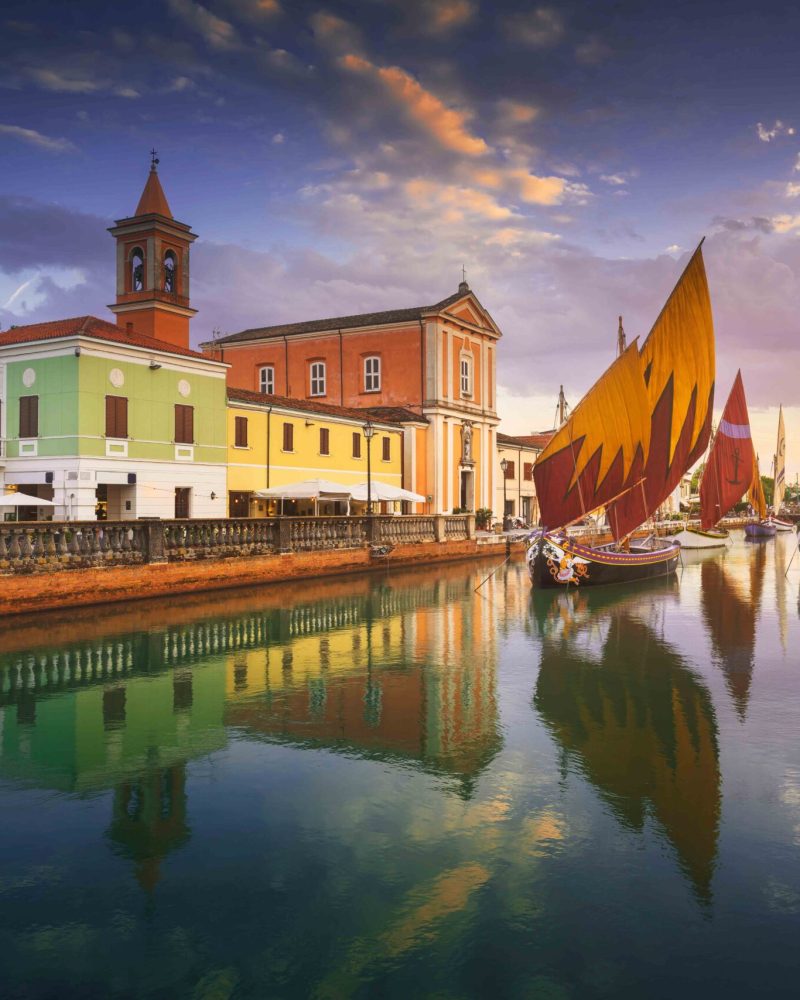 Cesenatico canal, historic wooden sailboats and church at sunset. Emilia Romagna region, Forlì Cesena province, Italy