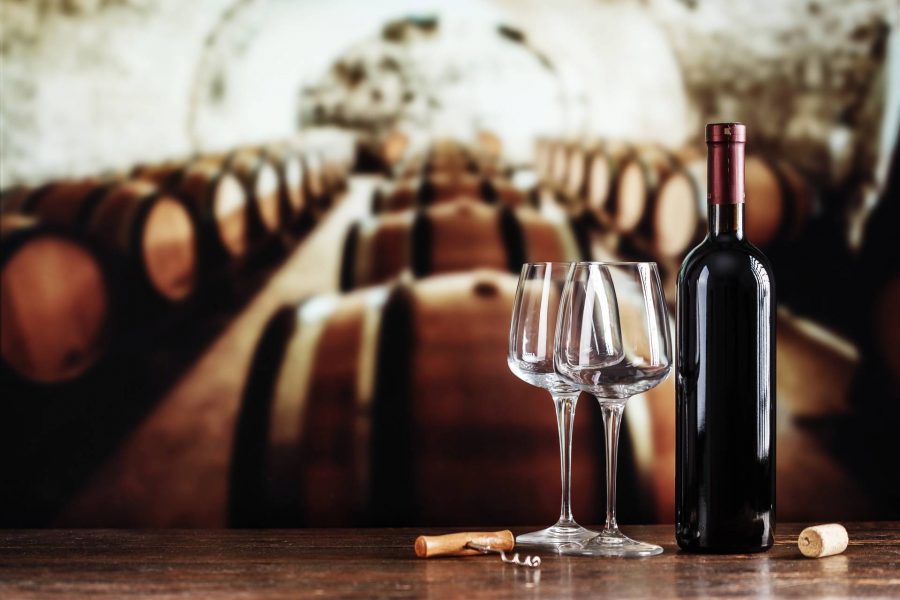a glass and a bottle of wine on the background of barrels in the cellar