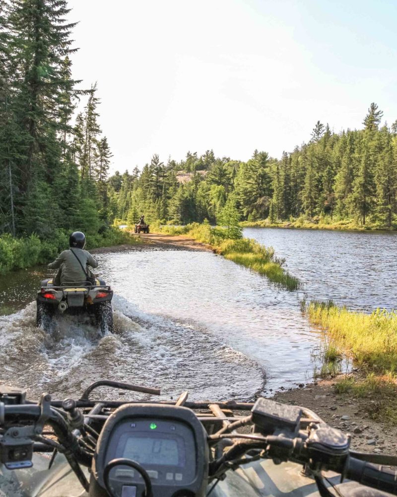 People driving ATV quadbike through water. Lake in Ontario, Canada.
