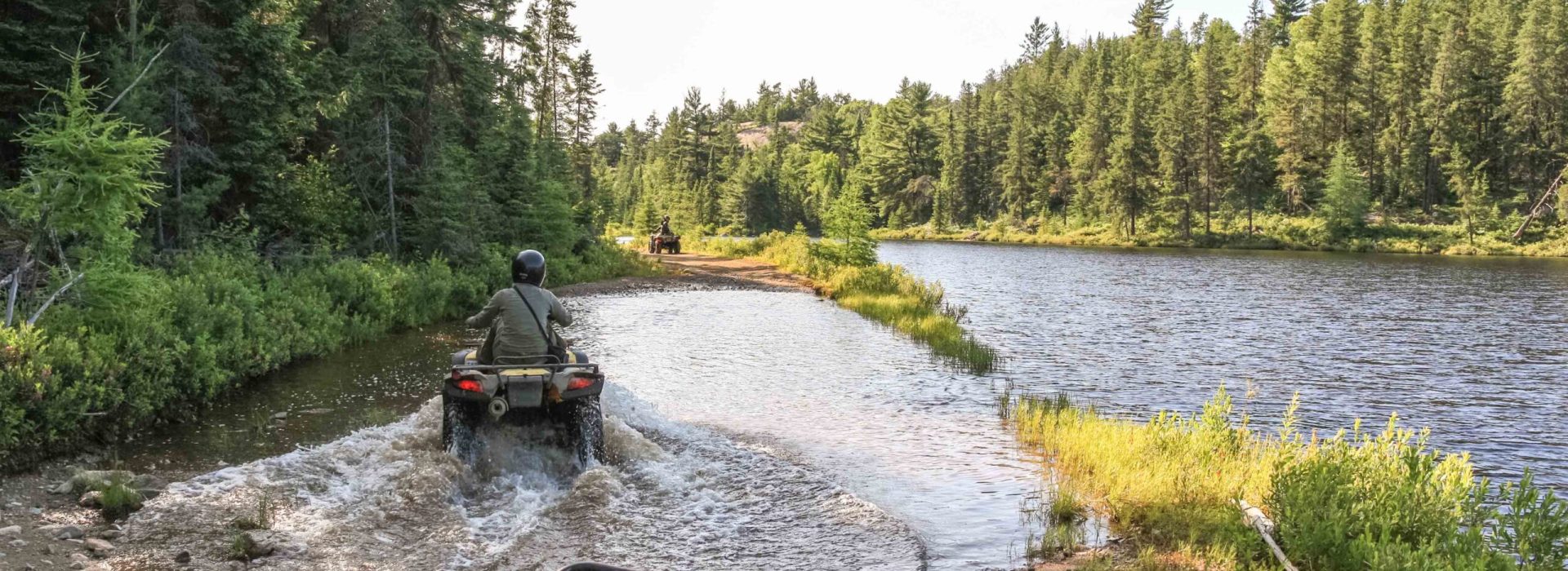 People driving ATV quadbike through water. Lake in Ontario, Canada.