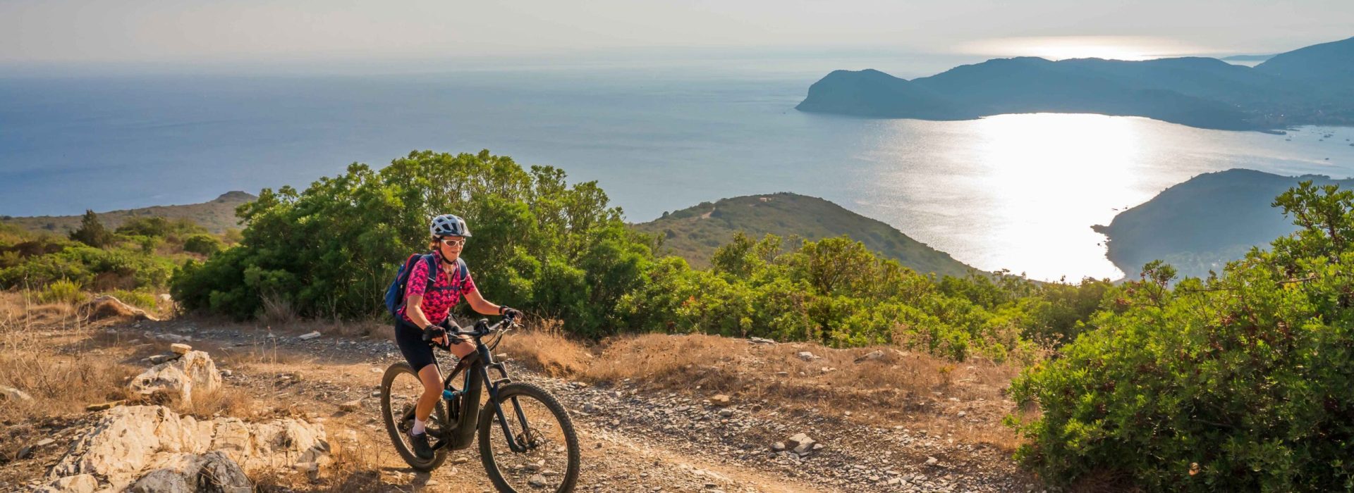 nice woman riding her electric mountain bike during sunset on the coastline above the mediterranean sea on the Island of Elba in the tuscan Archipelago, Tuscany, Italy