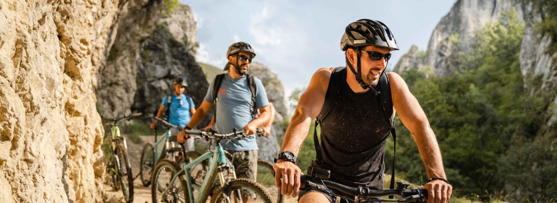 man caucasian male cyclist riding e-bike electric bicycle outdoor in mountain range at the gorge or ridge in front of his friends wear protective helmet and eyeglasses in sunny day copy space