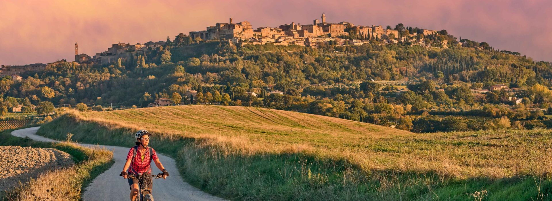 nice senior woman riding her electric mountain bike between olive trees in the Ghianti area with Montepulciano in background, Tuscany , Italy
