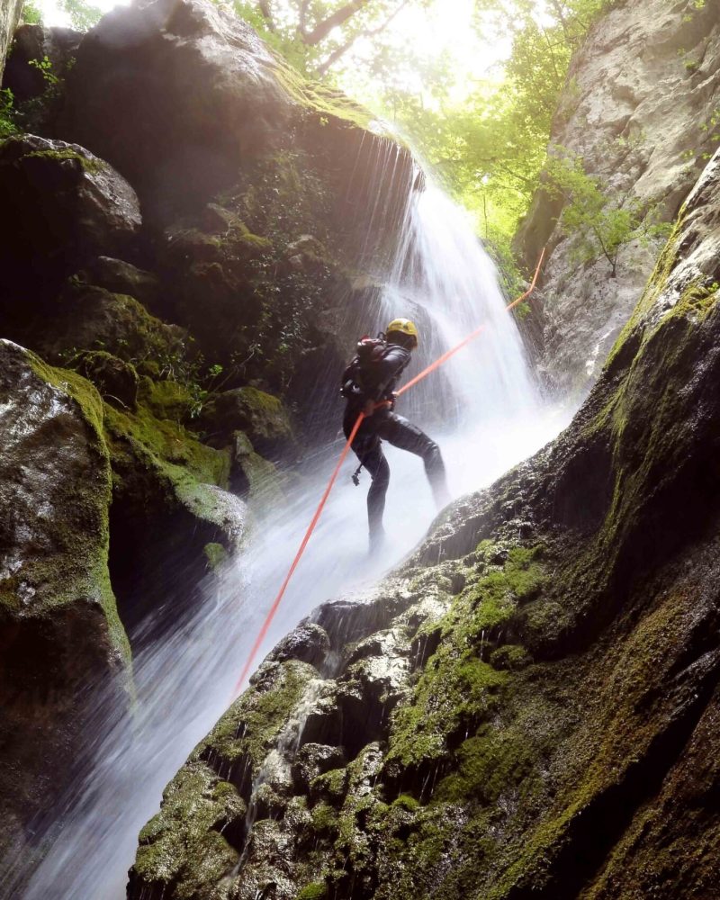 man rappelling down a waterfall backlit