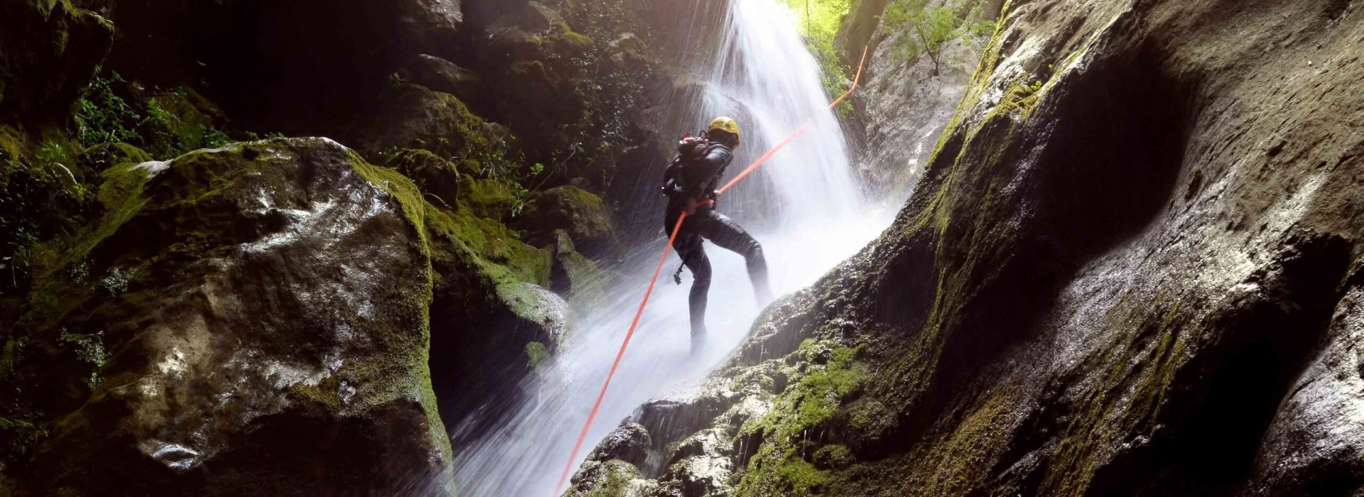man rappelling down a waterfall backlit